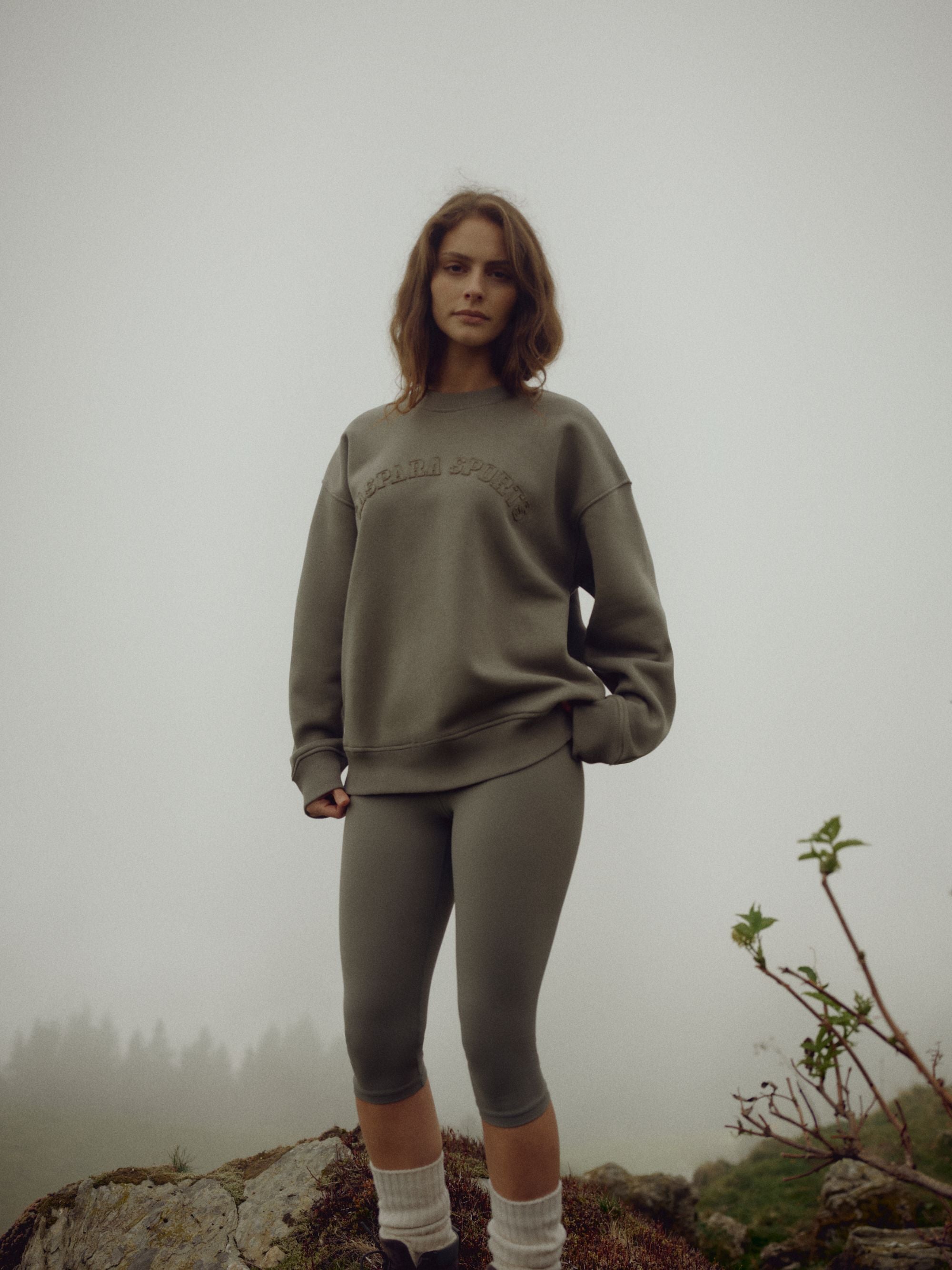 Woman wearing a khaki CASPARA CS crewneck sweatshirt on a foggy rocky hill.